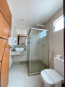 Interior view of a modern bathroom with beige tiled walls, a glass-enclosed shower, a white vessel sink on a floating counter, a toilet, and a wooden door.