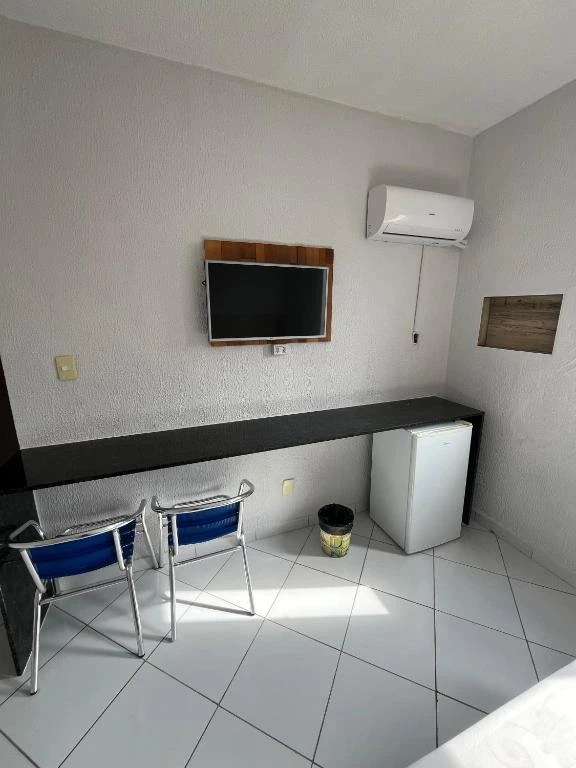 Functional hotel room corner featuring a long black desk, blue folding chairs, a wall-mounted flat-screen TV, AC unit, and a small mini-fridge.