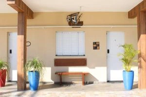 Inviting covered outdoor entrance area featuring warm beige walls, sturdy wooden pillars, large blue planters with greenery, and a wooden bench.
