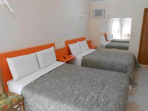Modern hotel room with two grey quilted beds, vibrant orange headboards, white walls, and a wall-mounted AC unit.