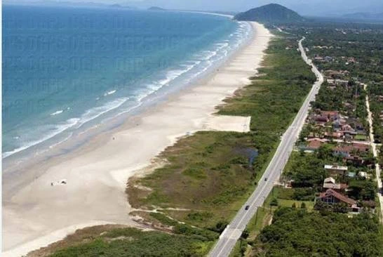 Ground-level view of crystal-clear, shallow turquoise water washing over smooth rocks on a sandy beach, framed by a lush green forested hill.