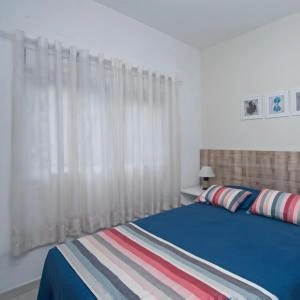 Cozy bedroom featuring a bed with a dark blue duvet and striped throw blanket, soft white curtains, and a tufted headboard.
