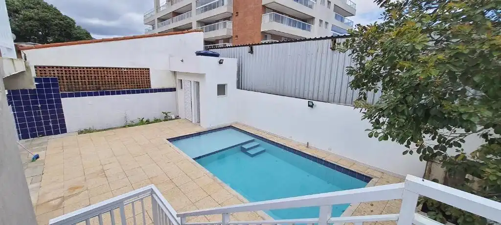 Small private backyard swimming pool with blue mosaic tiles, surrounded by a beige tiled deck and white privacy walls.