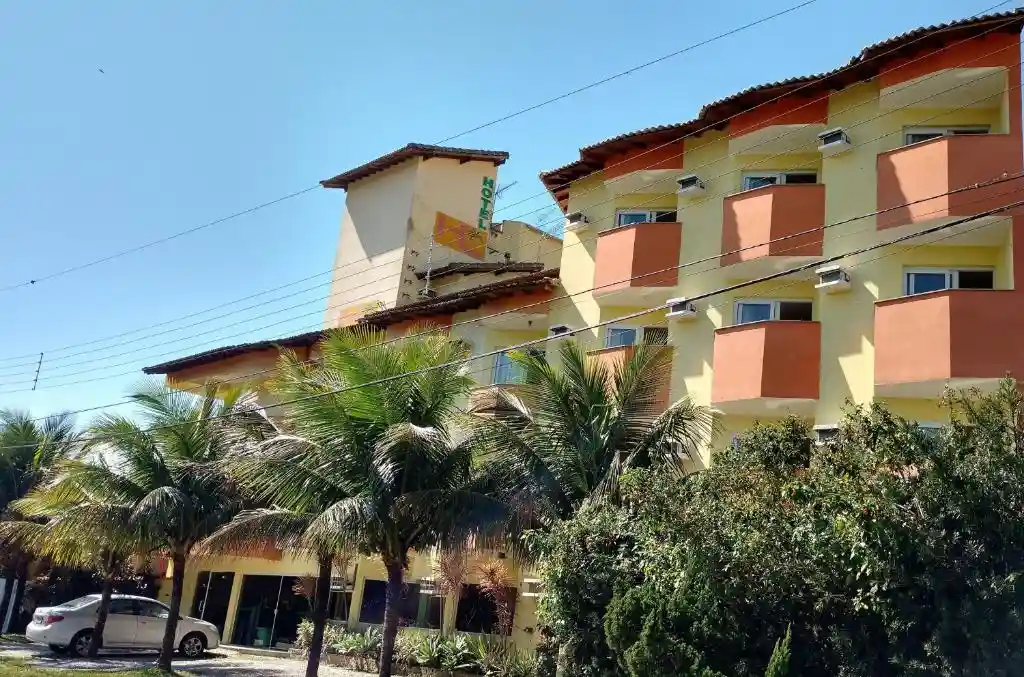 Multi-story yellow and orange hotel facade with private balconies, palm trees in front, and a car parked on the street.