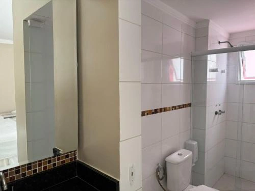 Modern white bathroom interior featuring a glass-door shower, white toilet, tall vanity mirror, and a decorative mosaic tile accent strip.