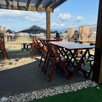 Sunny outdoor patio of Jolly Roger hostel, showing wooden furniture and a direct view of the sandy beach and ocean.
