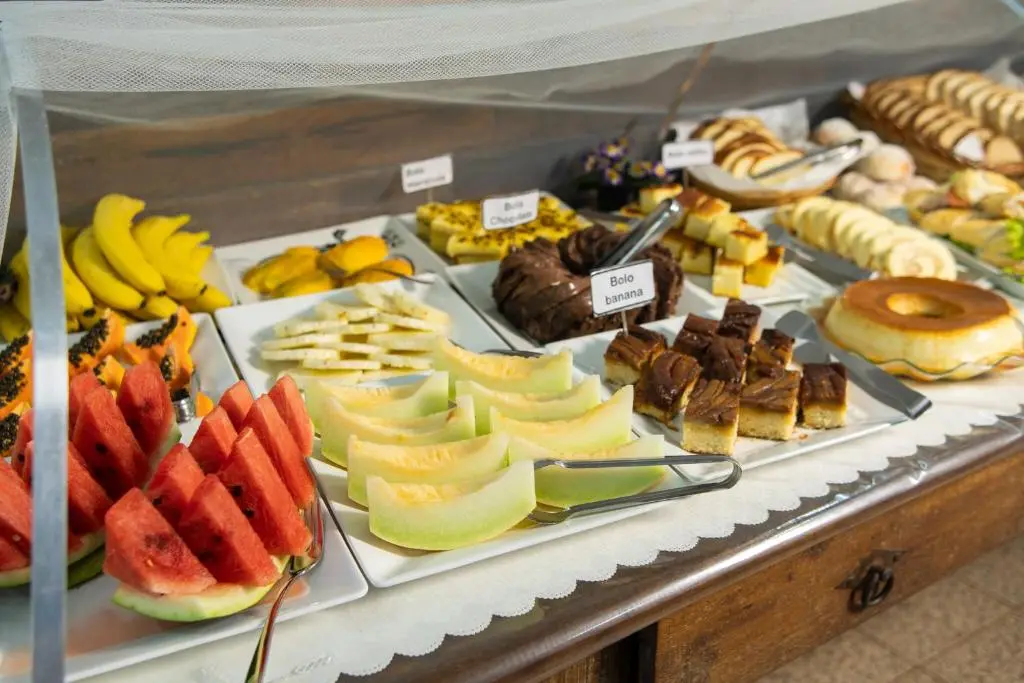 Close-up of a tropical breakfast selection featuring sliced watermelon, melon, banana, papaya, chocolate cake, and bread rolls.