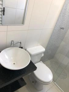 Clean, contemporary white bathroom interior featuring a dark vanity, a round white vessel sink, a standard toilet, and a modern glass shower stall.