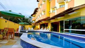 Resort-style outdoor swimming pool with blue water, white lounge chairs, green umbrellas, and a yellow hotel building in the background.