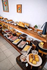 High-angle view of a breakfast buffet featuring a long wooden counter loaded with bread rolls, cakes, cold cuts, fruits, and a coffee machine on a tiled floor.