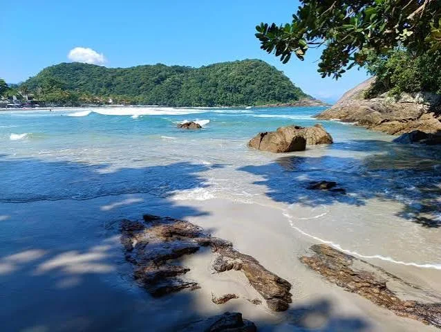 Wide panoramic aerial view of a massive sweeping crescent beach stretching toward a rocky headland, surrounded by green hills and blue ocean.