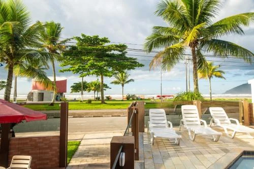 Relaxing outdoor pool deck with white sun loungers, palm trees, and a sweeping view of the ocean and sandy beach in the background.