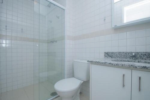 Clean bathroom interior with white tiled walls, a glass-enclosed shower, a toilet, and a white vanity topped with a speckled granite counter.