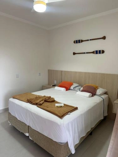 Interior of a cozy bedroom with a large double bed, white linens, orange and striped throw pillows, and decorative wooden paddles mounted on the wall.