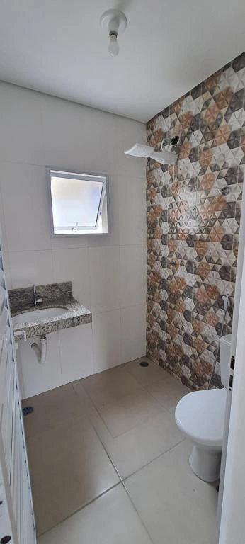 Modern bathroom interior featuring a decorative geometric tile shower wall, white toilet, and a wall-mounted stone sink under a high window.