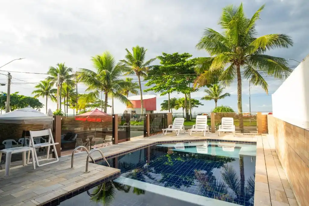 Private outdoor swimming pool with blue mosaic tiles, stainless steel handrails, white deck chairs, and palm tree reflections on the water.