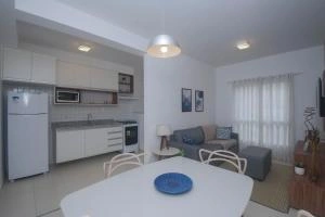 Bright open-concept apartment featuring a white kitchen, a white dining table with a blue plate, and a grey living room area in the background.