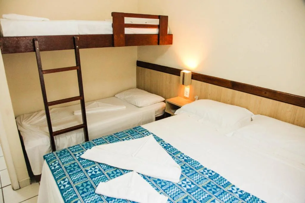 Interior view of a cozy family bedroom featuring a wooden bunk bed, a large double bed with a teal patterned runner, white towels, and warm wooden accents.