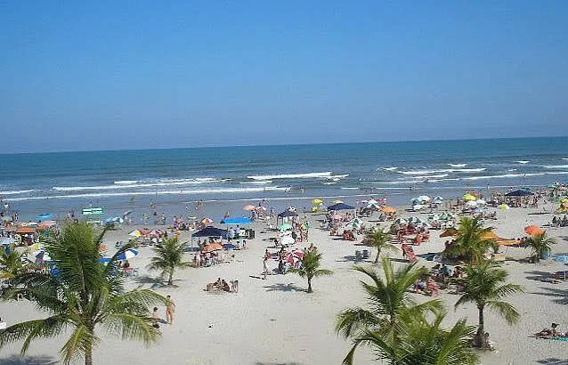 Peaceful, secluded beach scene featuring a wide stretch of white sand, a lush steep green mountain slope, and two small beach chairs with umbrellas.