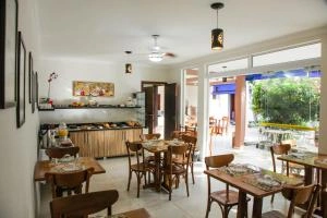 Interior view of a bright breakfast room with tiled floors, wooden tables and chairs, a buffet counter in the back, and large glass doors opening to the outdoor patio.