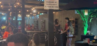 Nighttime view of Villa Caicara Boteco's rustic interior with warm string lights, patrons, and a hanging sign.