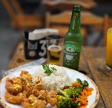 Close-up of fried shrimp, white rice, and vegetables served with a green Heineken beer bottle on a wooden table.