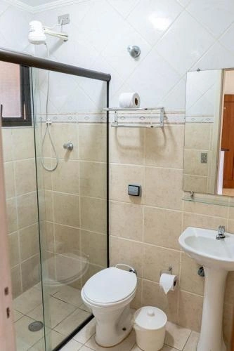 Clean white and beige tiled en-suite bathroom featuring a glass-door shower, white toilet, and porcelain pedestal sink.