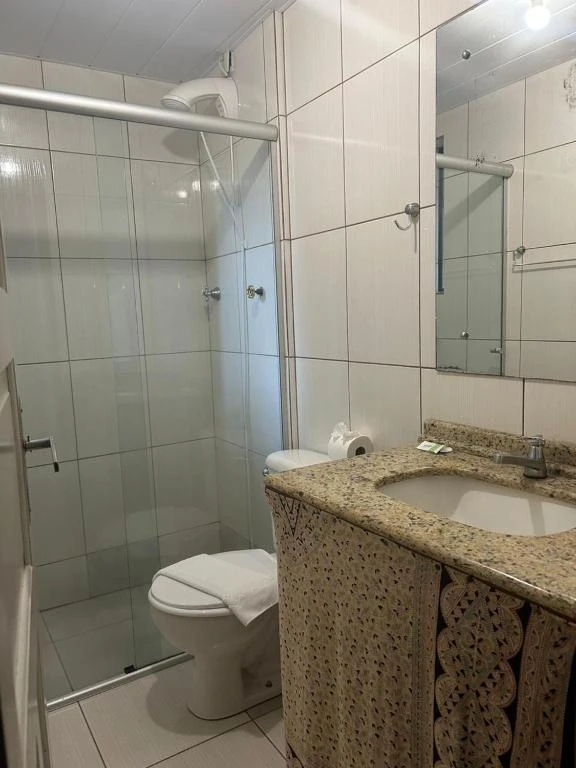 Small modern bathroom featuring white wall tiles, a glass-enclosed shower, a toilet, and a granite vanity sink with a textured skirt.