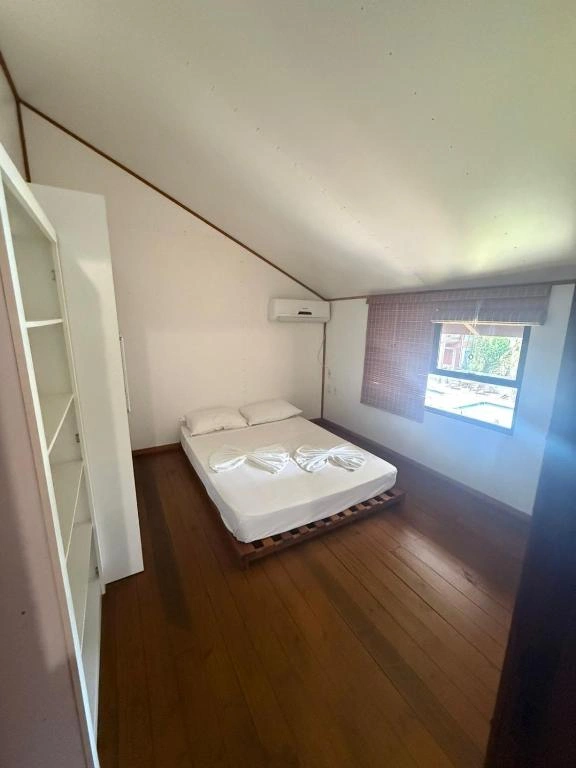 Bright attic bedroom with white walls, a sloped ceiling, wooden flooring, a white wardrobe, and a bed with neatly folded towels.