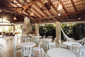Large open-air dining pavilion featuring a thatched roof, exposed wooden beams, brick pillars, and white round tables with matching chairs.