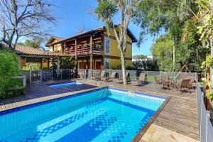 Outdoor rectangular swimming pool with a wooden deck, sun loungers, and a yellow two-story house with a balcony in the background.