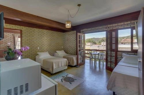Room featuring three single beds, exposed brick walls, wooden beams, a turtle rug, and open French doors leading to a balcony with mountain views.