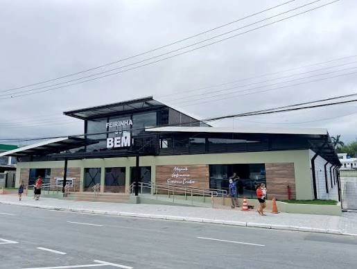 A modern, multi-level commercial building with a glass and metal facade, black columns, and wooden panel accents, located next to a paved street.