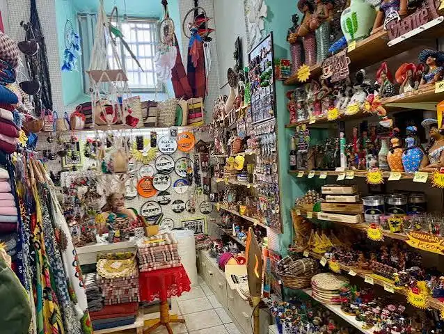 An interior shot of a dense, colorful boutique packed with novelty fridge magnets, trinkets, postcards, and regional souvenirs on overflowing shelves.