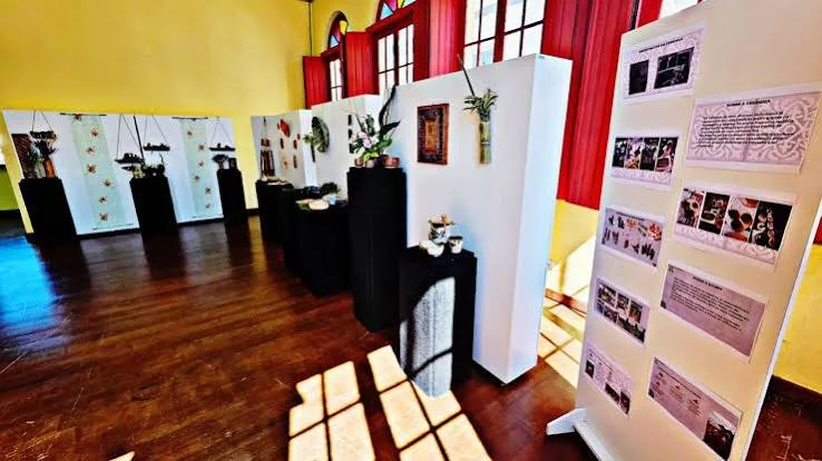 A well-lit exhibition space with yellow walls, dark wooden floors, tall display panels, and photographs detailing local history and culture.