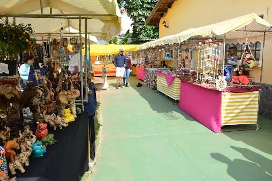A row of outdoor souvenir stalls under yellow canopies displaying wooden carvings, toys, and artisan goods on green-painted walkways.