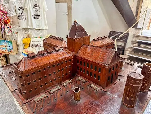A highly detailed, handcrafted miniature wooden model of a large historical building displayed on a table in a shop.