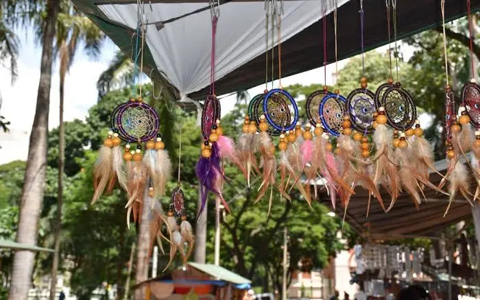 A close-up view of colorful, handcrafted dreamcatchers with feathers and beads hanging from the canopy of an outdoor market stall.