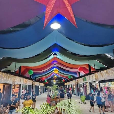 A bustling indoor mall corridor adorned with a massive red star, vibrant blue and rainbow ceiling drapes, and brightly lit storefronts.