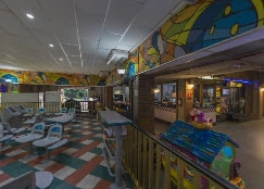 A vibrant indoor family entertainment area featuring whimsical aquatic-themed wall murals, a checkered floor, and modern seating, situated next to a bowling alley.