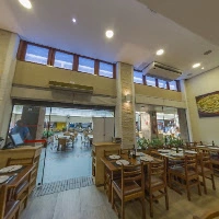 A spacious, well-lit casual dining restaurant interior with high ceilings, large windows, wooden tables, and a clear view of the open patio area.
