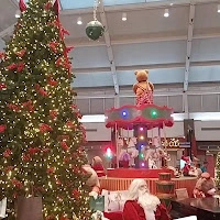 A festive mall event area featuring a large decorated Christmas tree, a Santa figure, and a colorful performance stage setup.