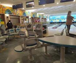 A clear view of a modern bowling alley with sleek lanes, vibrant lighting, and colorful seating area with a railing.