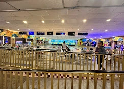 An elevated view of a bowling alley and entertainment center featuring gold railings, neon lighting, and arcade cabinets.