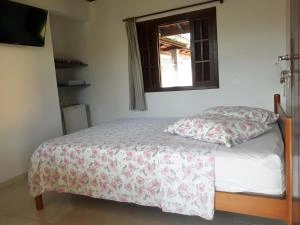 Relaxing bedroom featuring a double bed with pink floral bedding, wooden frame, wall-mounted TV, and a window with wooden shutters.
