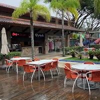 An inviting outdoor dining patio featuring bright orange chairs and white tables set on a wooden deck, surrounded by lush palm trees and shops.