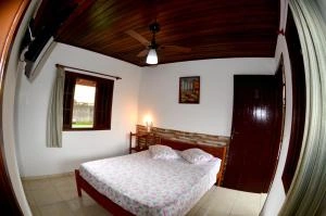 Charming rustic bedroom with dark wood ceiling, ceiling fan, double bed with floral linens, and a window with wooden shutters.