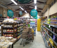 A well-stocked grocery store aisle featuring aisles of packaged goods, fresh baked bread, and promotional sale signs overhead.