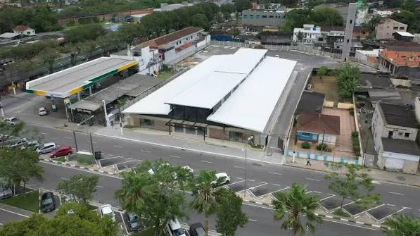 A high-angle aerial shot showing a large white-roofed commercial building situated next to a gas station, parking lot, and a main road.
