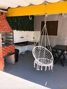 A covered outdoor kitchen area with a brick barbecue grill, sink, and a hanging white wicker chair.